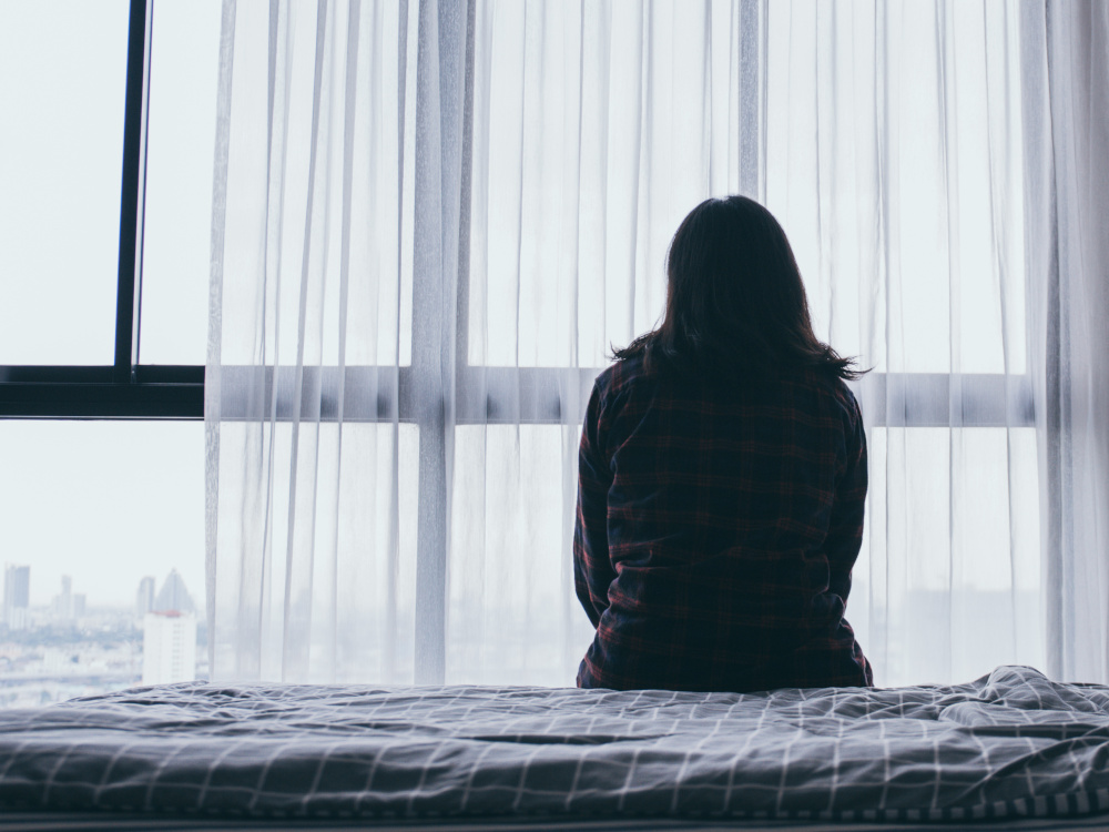 Picture of woman sitting alone on a bed looking out the window